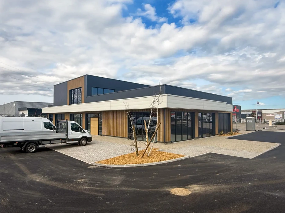 Extérieur d'un bâtiment industriel en construction avec bardage métallique blanc, plusieurs ouvertures de grande hauteur pour portes sectionnelles, fenêtres rectangulaires réparties sur la façade