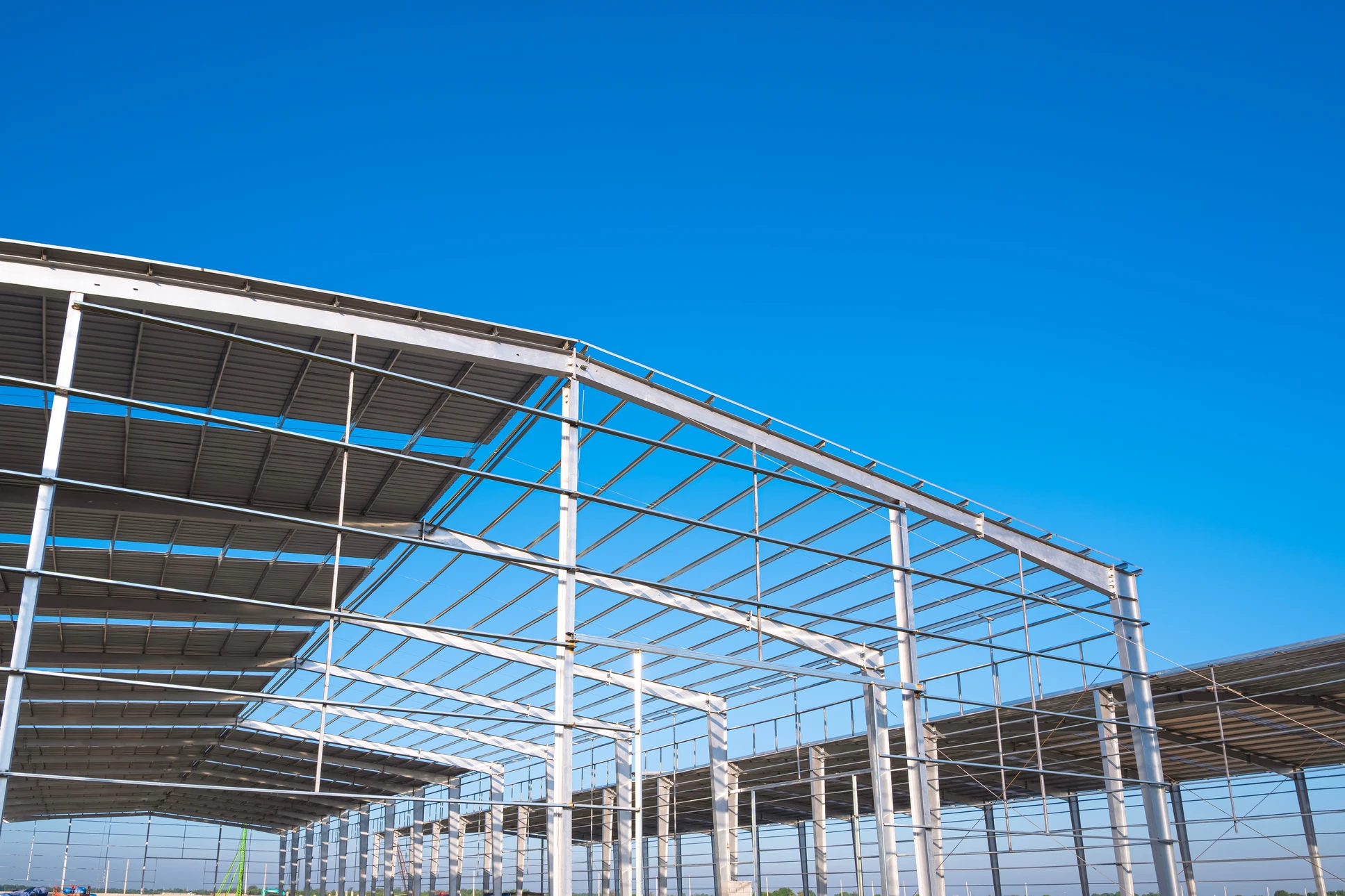 Structure métallique industrielle photographiée en contre-plongée, montrant un assemblage complexe de poutrelles d'acier galvanisé formant une charpente ou pylône