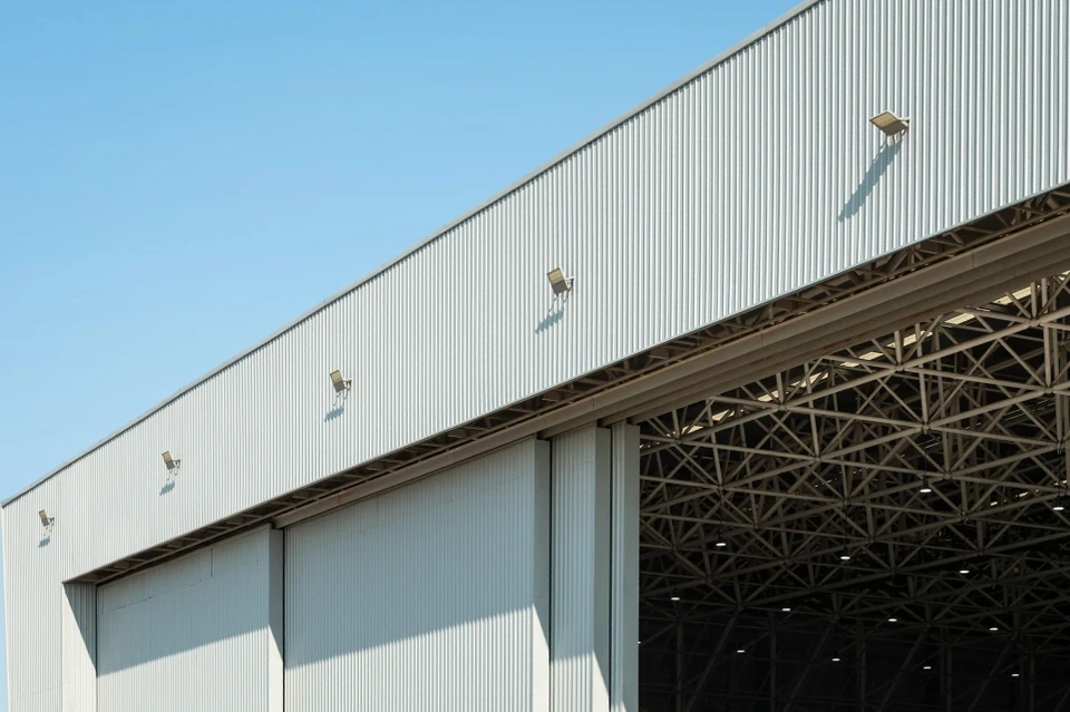 Façade d'immeuble commercial moderne avec logo d'entreprise "Les Mousquetaires" en relief rouge et blanc sur panneau de verre teinté bleu foncé